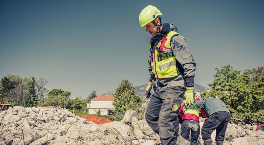 Emergency responders in protective gear searching through rubble in a disaster zone.